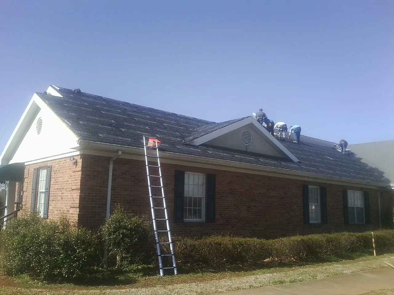 Crew tearing shingles off a brick ranch roof with a ladder set — Metal Roof Repair work by our crew in Eaton