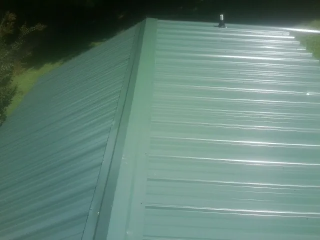 New green metal panels meeting at the ridge of a roof — Flat Roof Repair work by our crew in Eaton
